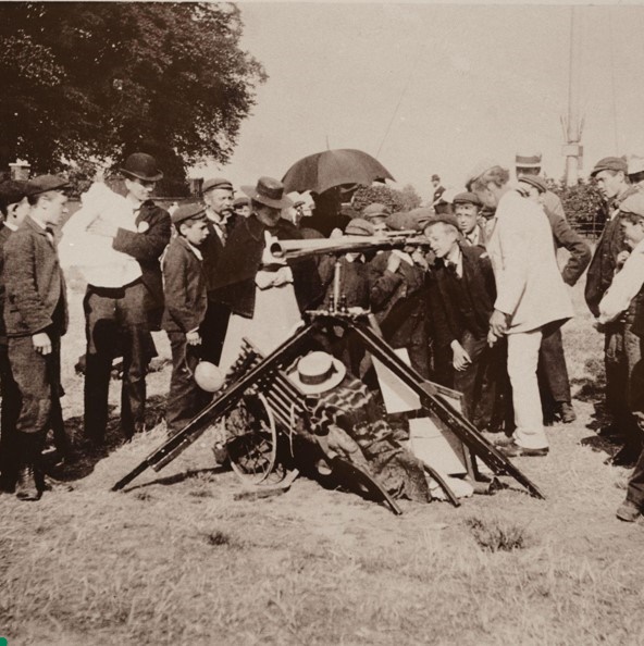 A photograph of a crowd gathering round a boy looking through a telescope. 